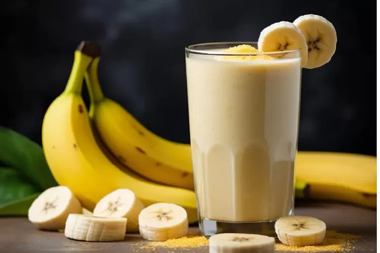 Segelas smoothie pisang creamy yang dihiasi irisan pisang segar dan taburan granola untuk tampilan menarik